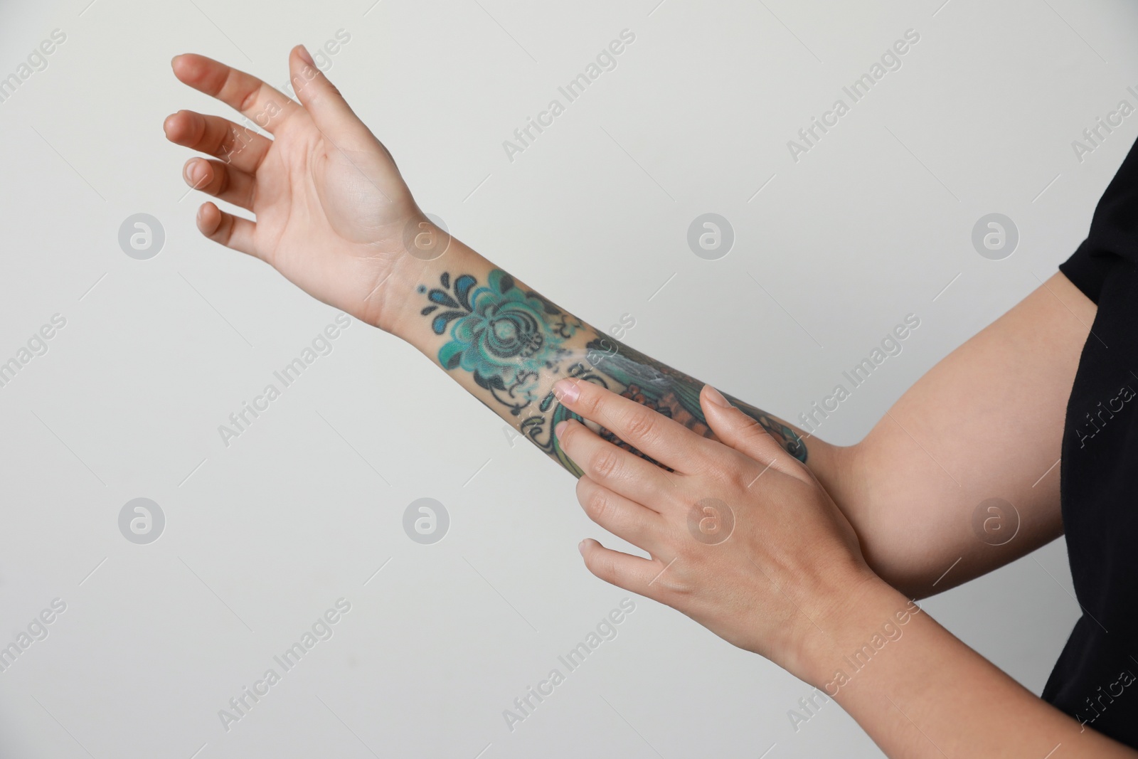 Photo of Woman applying cream on her arm with tattoos against light background, closeup