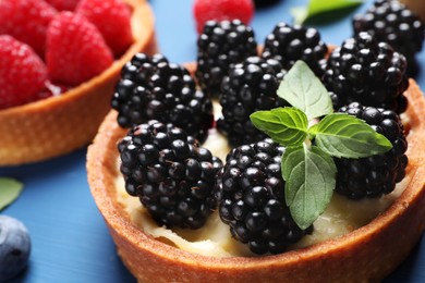 Photo of Tartlet with fresh blackberries and mint on blue table, closeup. Delicious dessert
