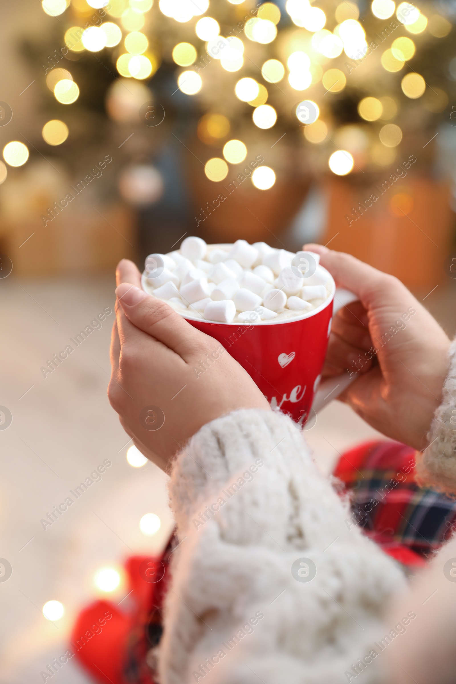 Photo of Woman holding cup of hot drink with marshmallows indoors, closeup. Magic Christmas atmosphere