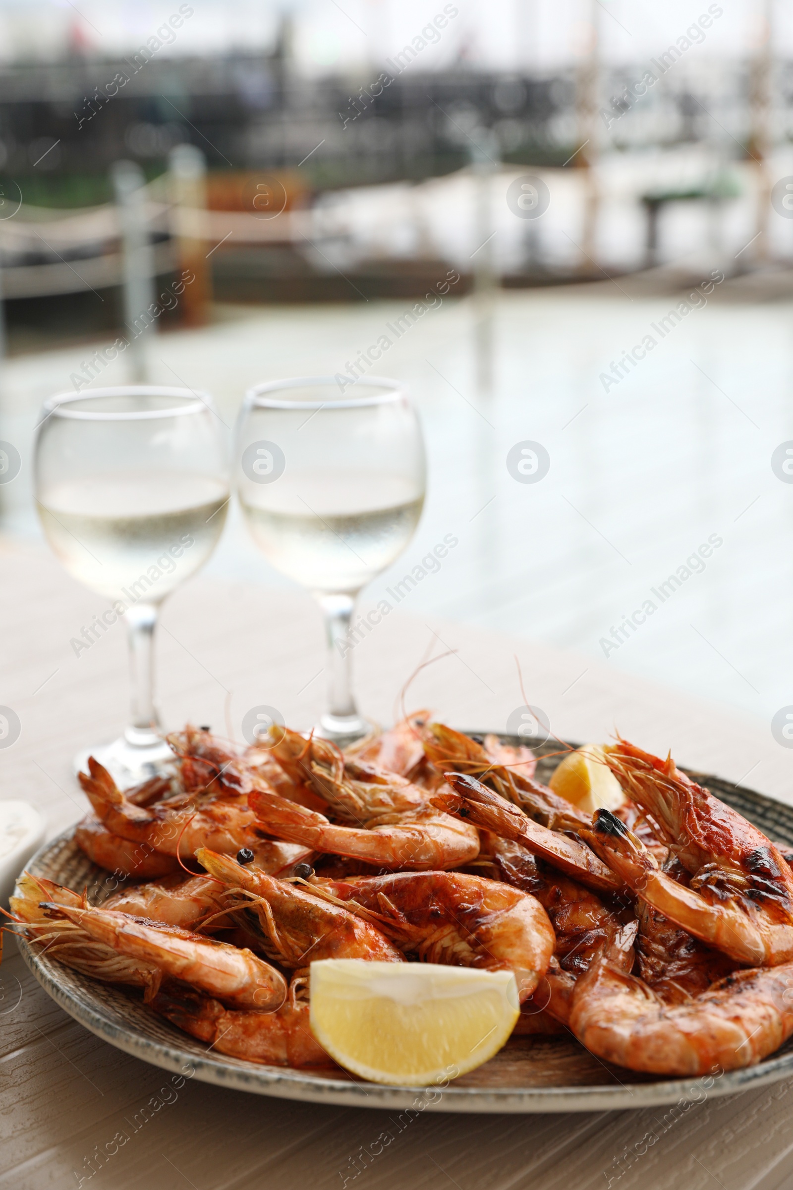 Photo of Plate of delicious cooked shrimps served with lemon and wine at table outdoors