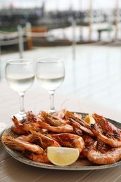 Photo of Plate of delicious cooked shrimps served with lemon and wine at table outdoors