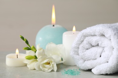 Photo of Beautiful spa composition with burning candle, rolled towel and flowers on white table