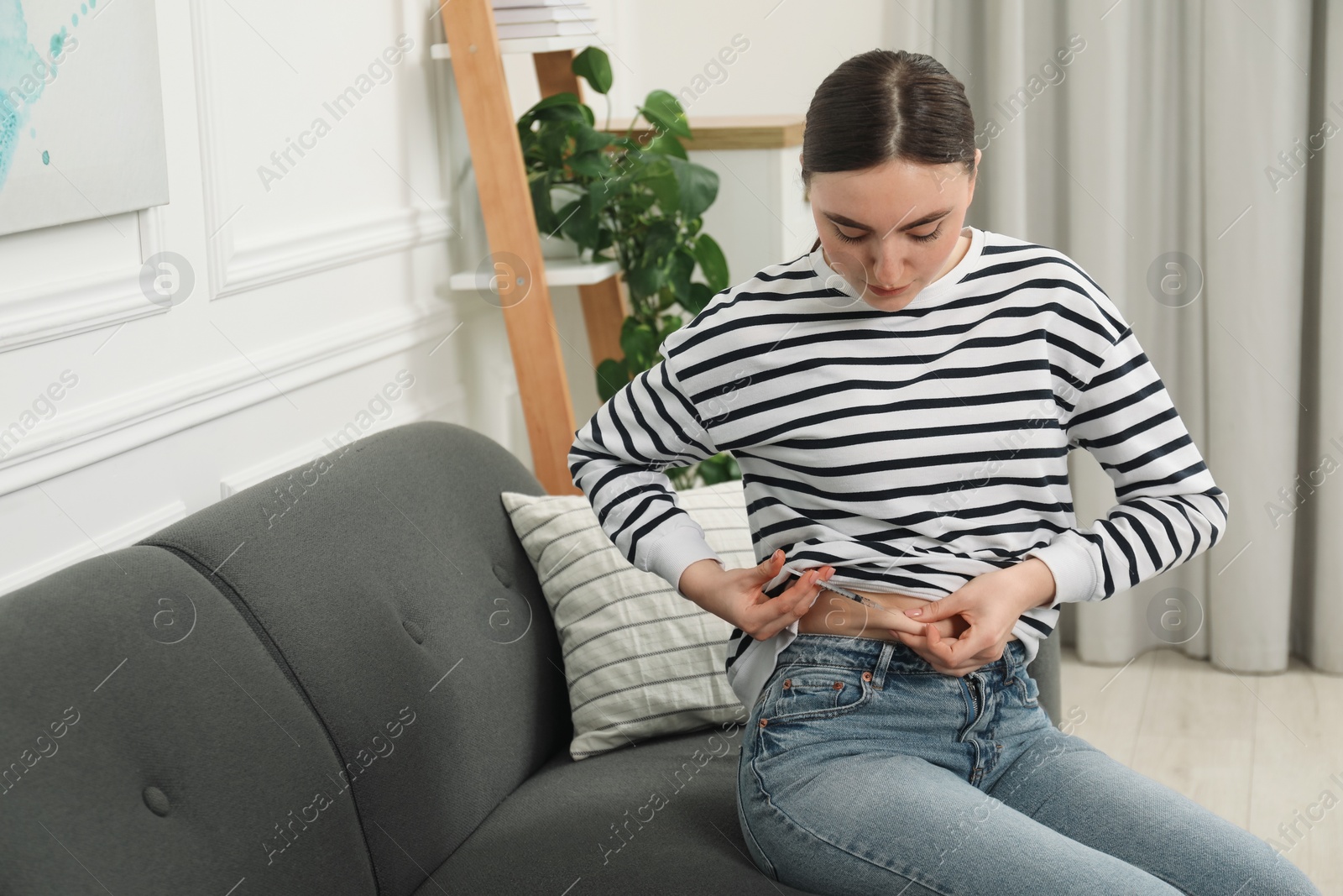 Photo of Diabetes. Woman making insulin injection into her belly on sofa at home