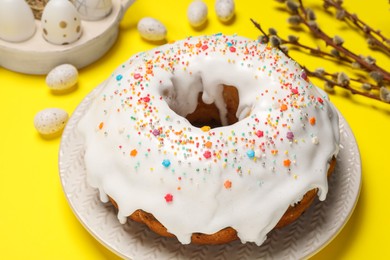 Photo of Easter cake with sprinkles, painted eggs and willow branches on yellow background