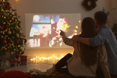 Photo of Couple watching Christmas movie via video projector in cosy room, back view. Winter holidays atmosphere