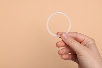 Photo of Woman holding diaphragm vaginal contraceptive ring on beige background, closeup. Space for text