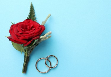 Small stylish boutonniere and rings on light blue background, top view. Space for text