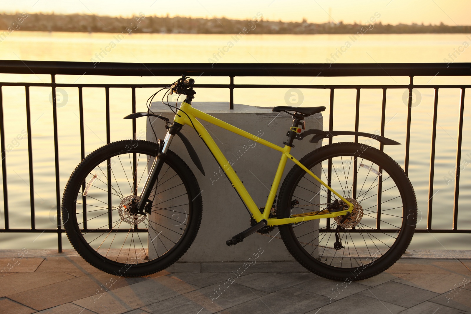 Photo of Yellow bicycle parked near railing on city waterfront at sunset