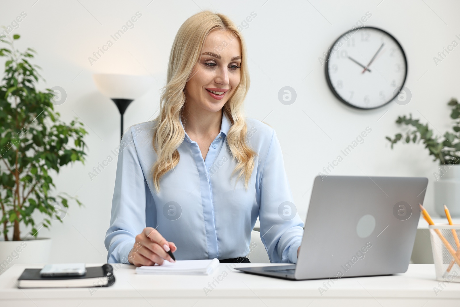Photo of Happy secretary taking notes while working with laptop in office