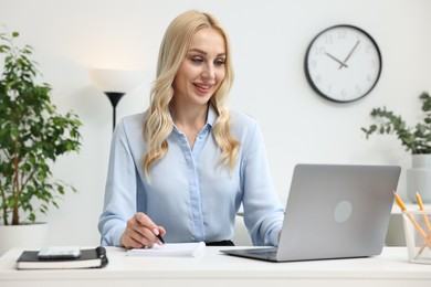 Happy secretary taking notes while working with laptop in office