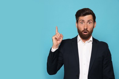 Photo of Surprised bearded man pointing index fingers up on light blue background. Space for text