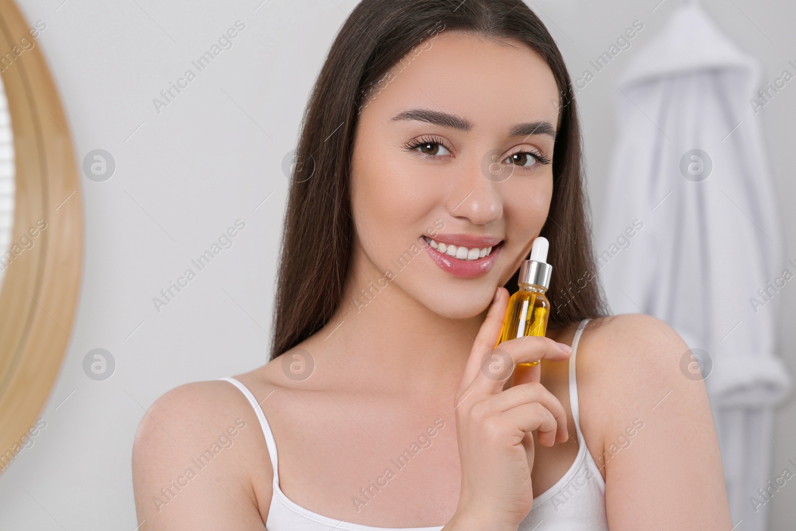 Photo of Happy young woman with bottle of essential oil in bathroom