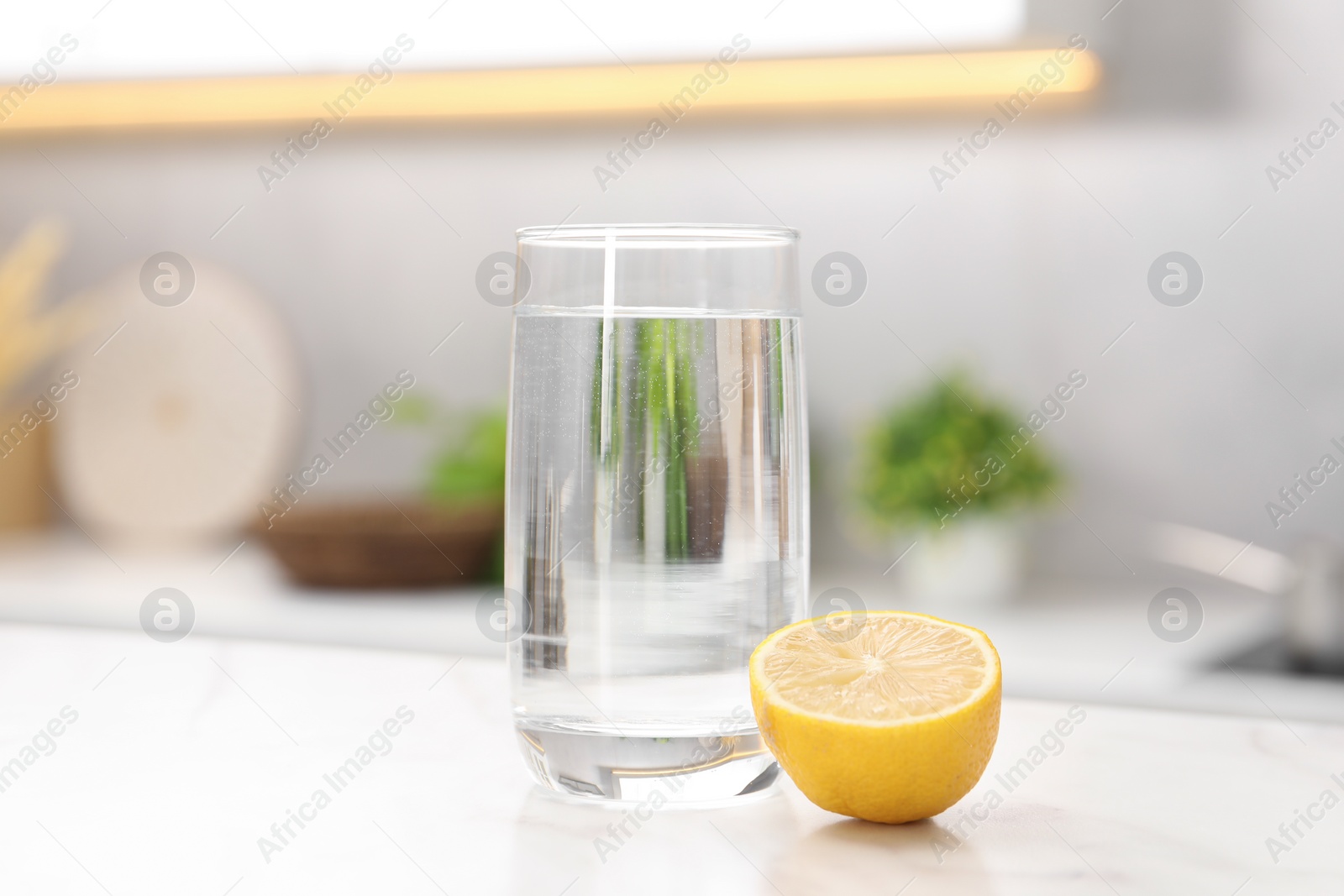 Photo of Glass with clear water and half of lemon on white table in kitchen