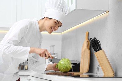 Photo of Professional chef cutting cabbage at white countertop in kitchen