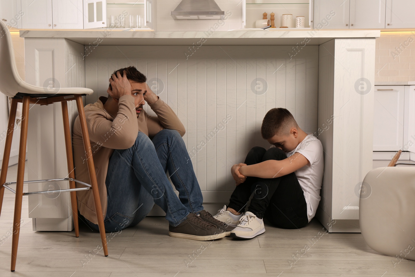 Photo of Father and his son hiding under table in kitchen during earthquake