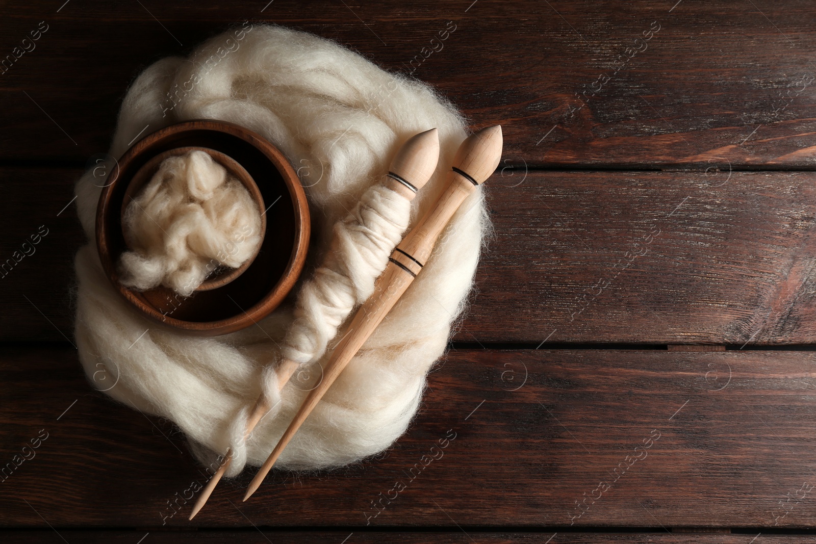 Photo of Soft white wool and spindles on wooden table, top view. Space for text