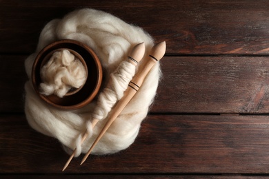 Soft white wool and spindles on wooden table, top view. Space for text