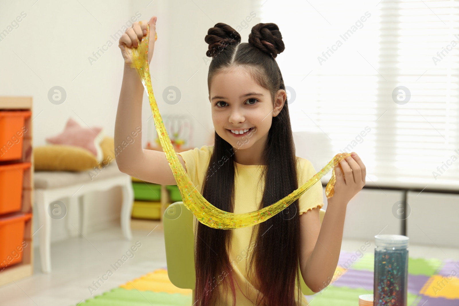 Photo of Little girl playing with slime in room