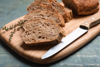 Cut buckwheat baguette with knife and thyme on light blue wooden table, closeup