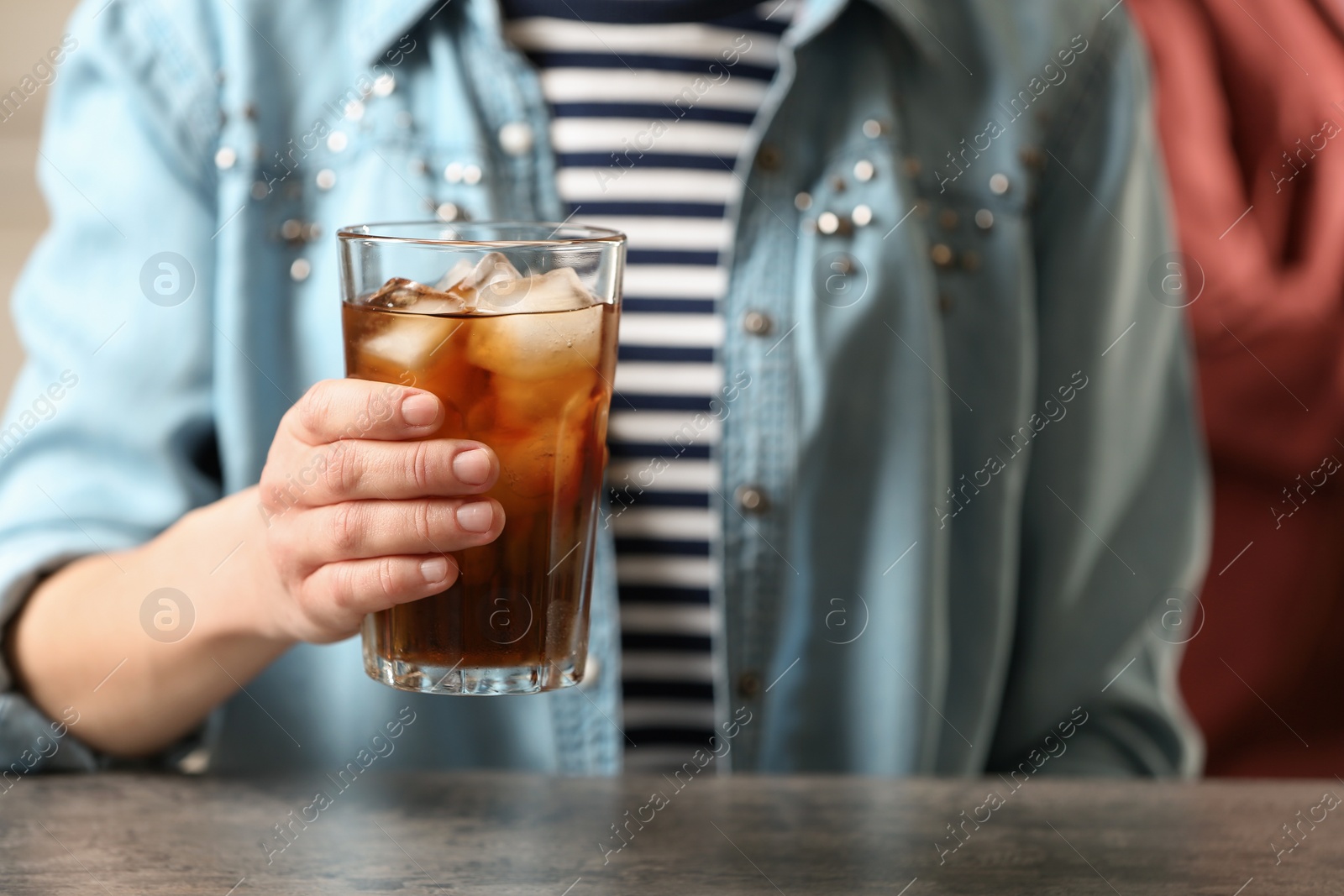 Photo of Woman holding glass of cola with ice at table, closeup