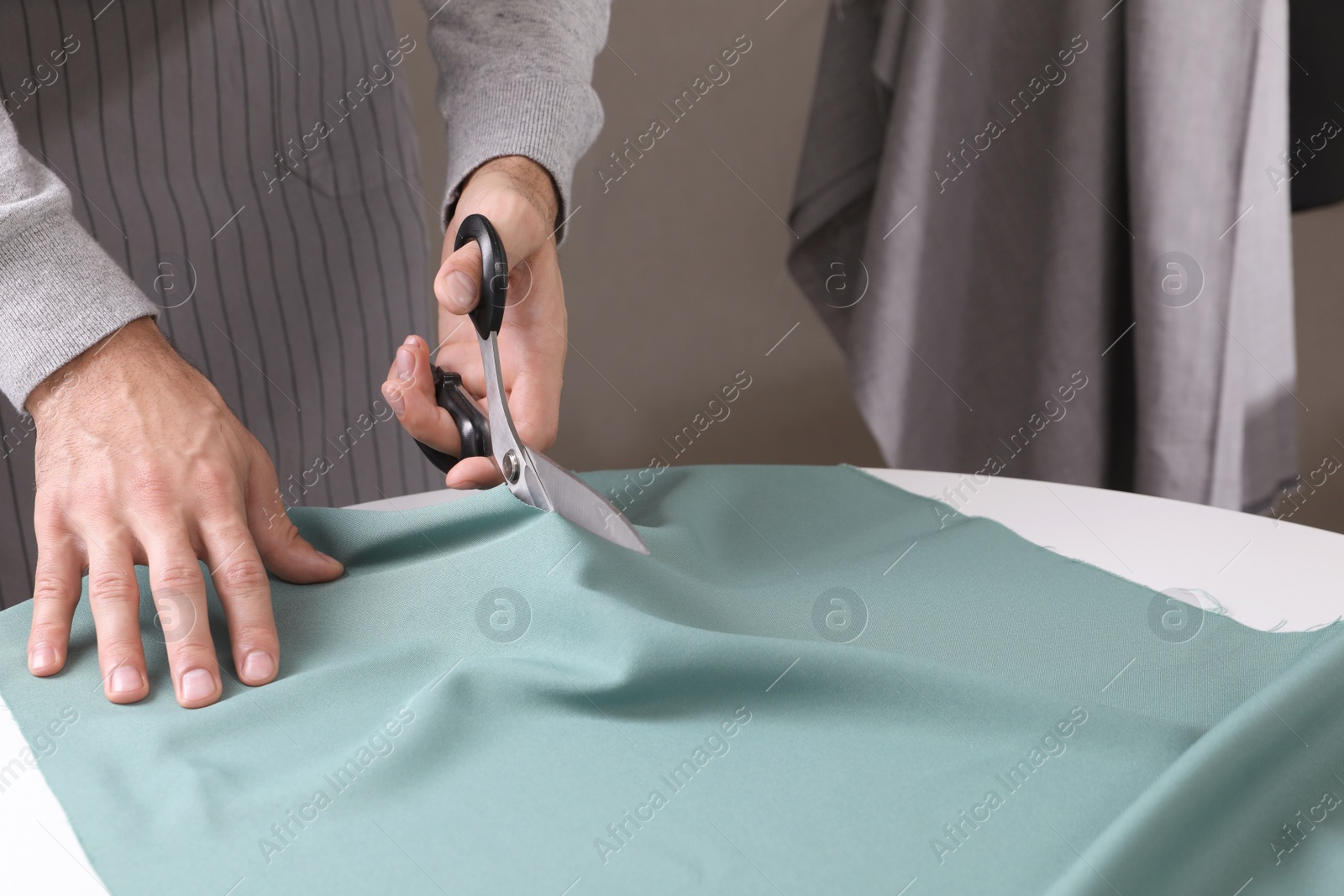 Photo of Tailor cutting fabric with scissors at table in atelier, closeup