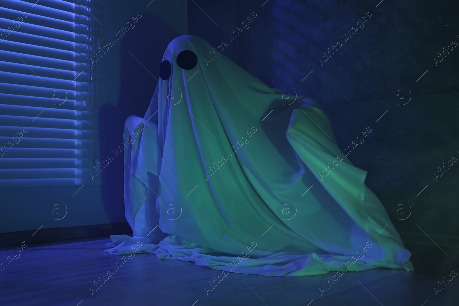 Photo of Creepy ghost. Woman covered with sheet near window in blue light