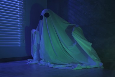 Photo of Creepy ghost. Woman covered with sheet near window in blue light