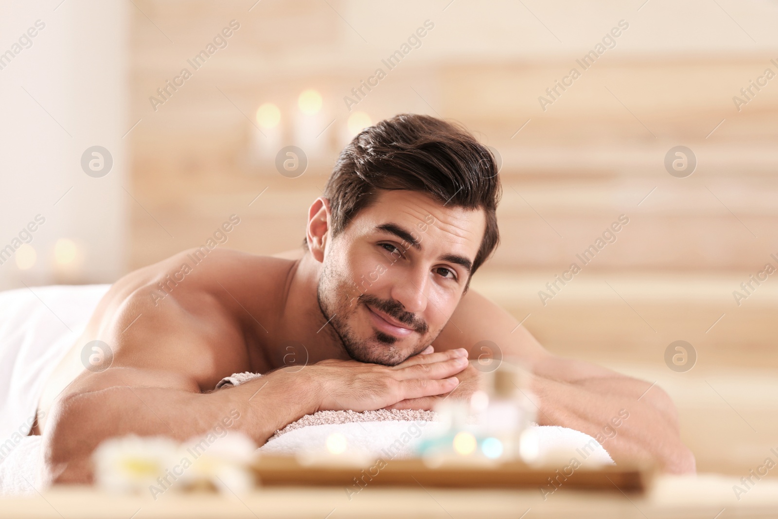 Photo of Handsome young man relaxing on massage table in spa salon, space for text