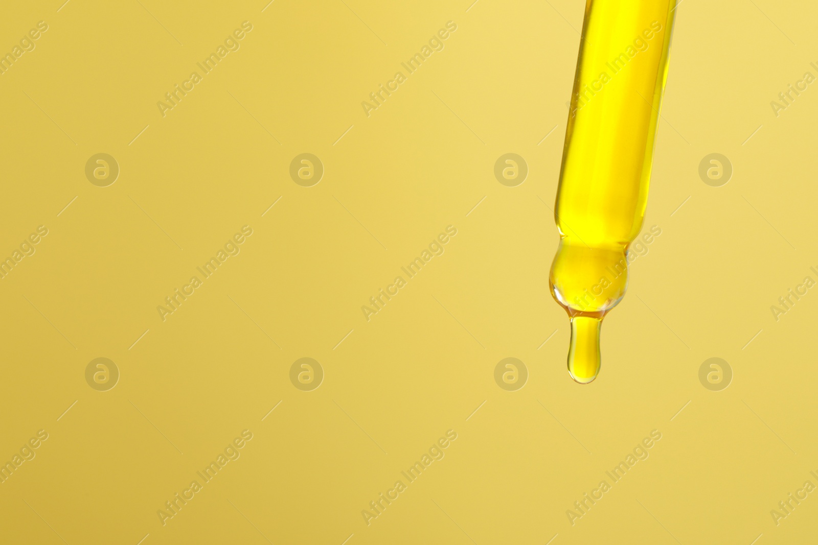 Photo of Dripping serum from pipette on yellow background, closeup. Space for text