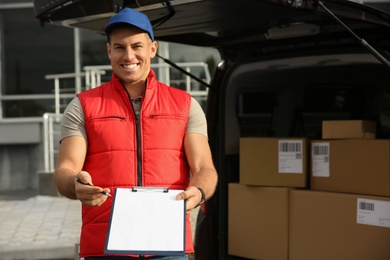 Courier with clipboard near car full of packages outdoors