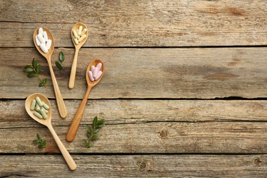 Photo of Vitamin capsules in spoons and leaves on wooden table, flat lay. Space for text