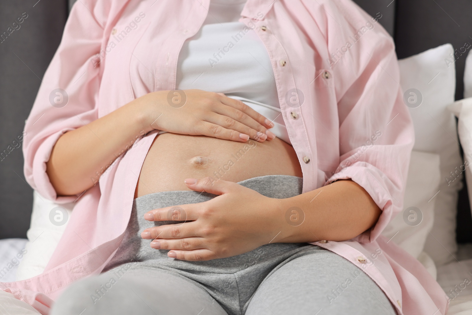 Photo of Pregnant woman in pink shirt lying on bed, closeup