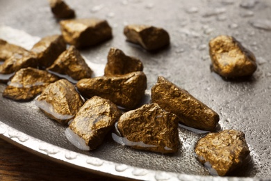 Photo of Plate with gold nuggets and water on table, closeup