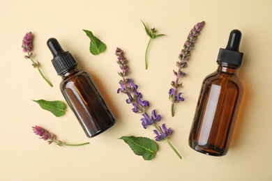 Photo of Bottles of essential oil and sage flowers on color background, flat lay