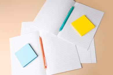 Photo of Copybooks with erasable pens and paper notes on beige background, above view