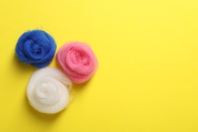 Colorful felting wool on yellow background, flat lay. Space for text