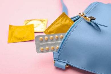 Photo of Purse with condoms and birth control pills on pink background. Safe sex