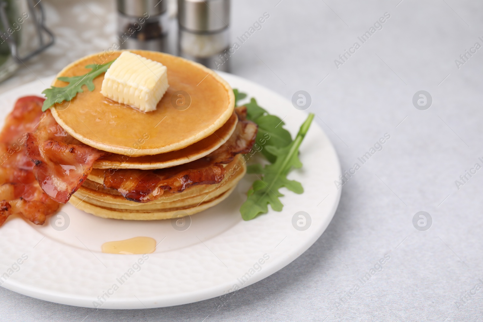 Photo of Delicious pancakes with bacon, butter and arugula on light table, closeup. Space for text