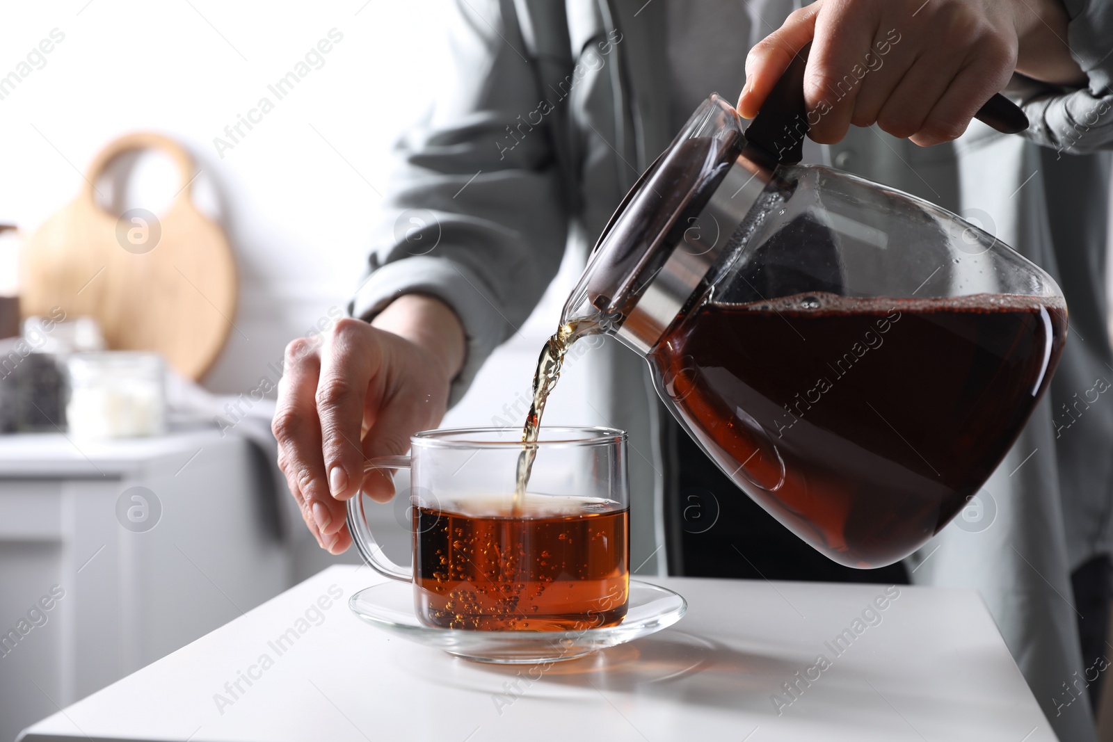 Photo of Woman pouring hot tea into cup at white table, closeup