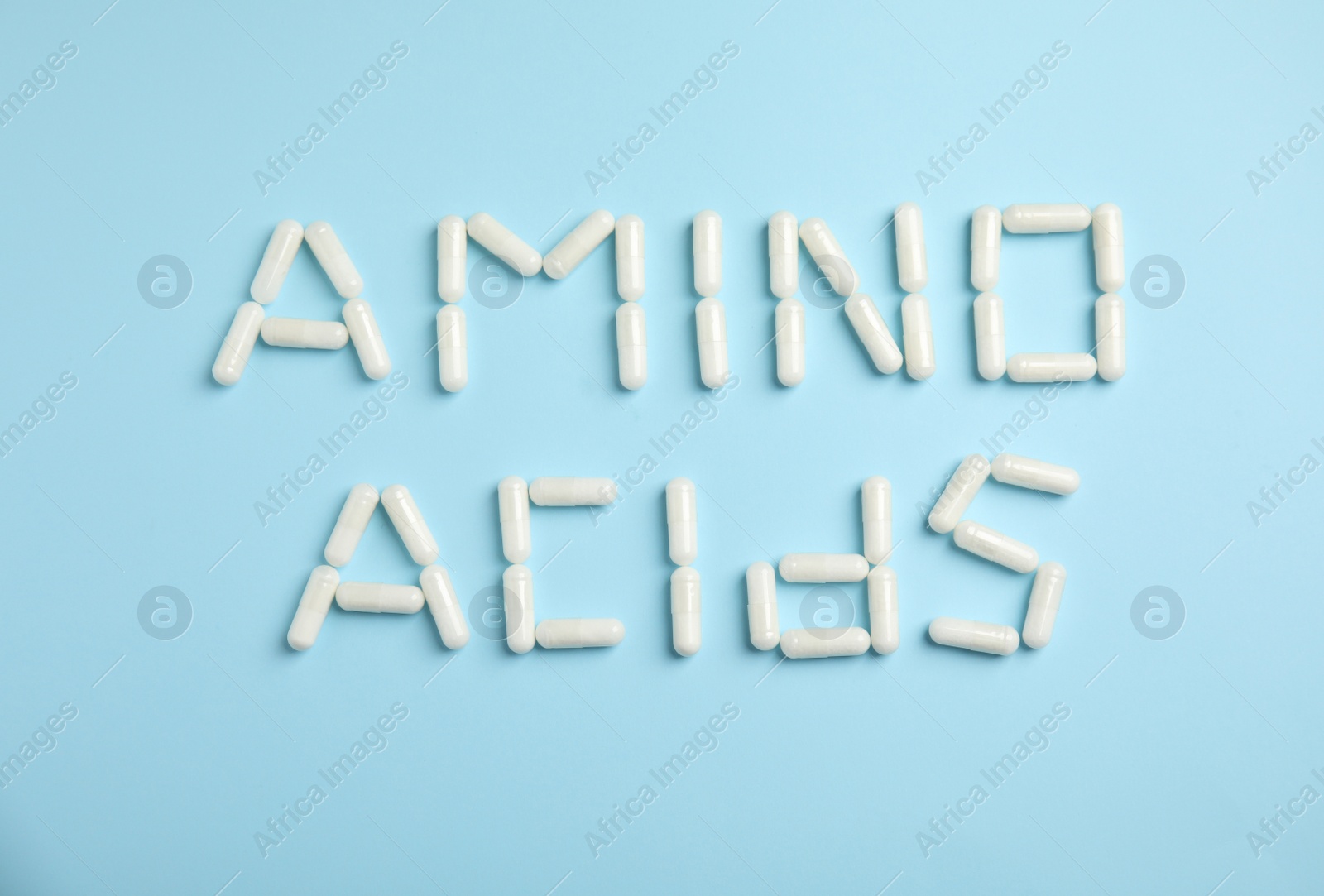 Photo of Phrase Amino acids made of pills on light blue background, flat lay