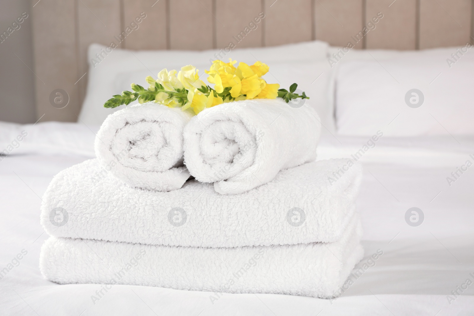 Photo of Fresh white towels with flower on bed indoors