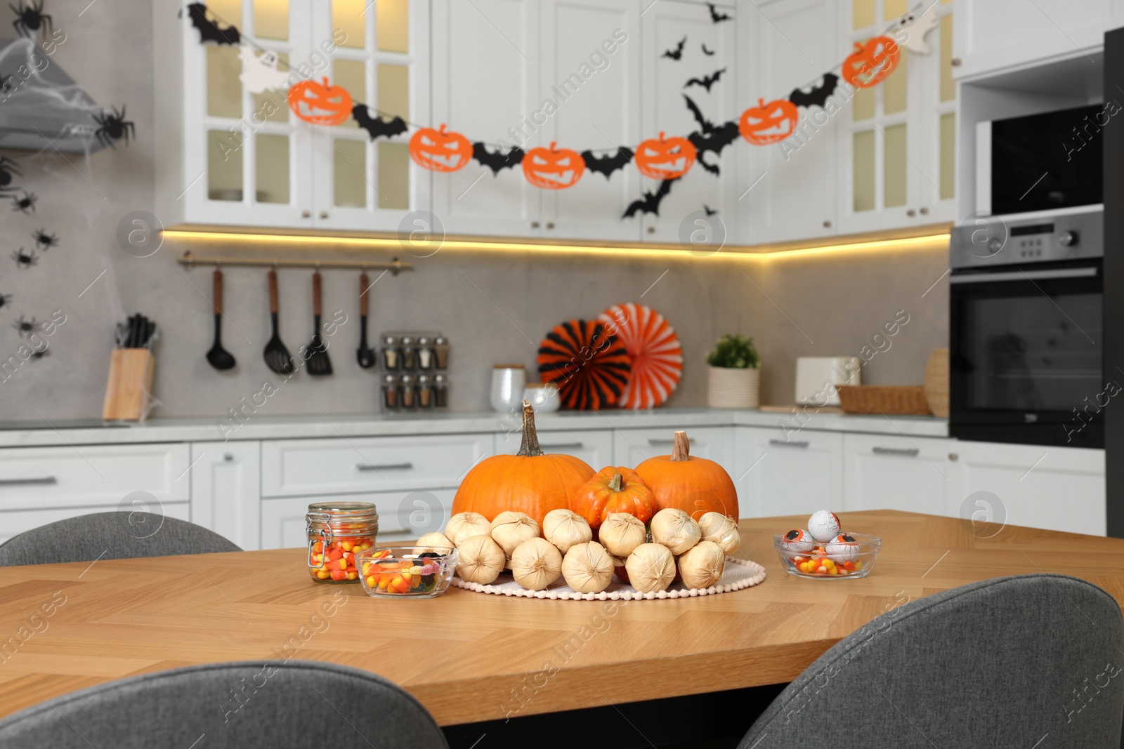 Photo of Kitchen decorated for Halloween. Pumpkins, jelly candies and bunch of garlic on wooden table