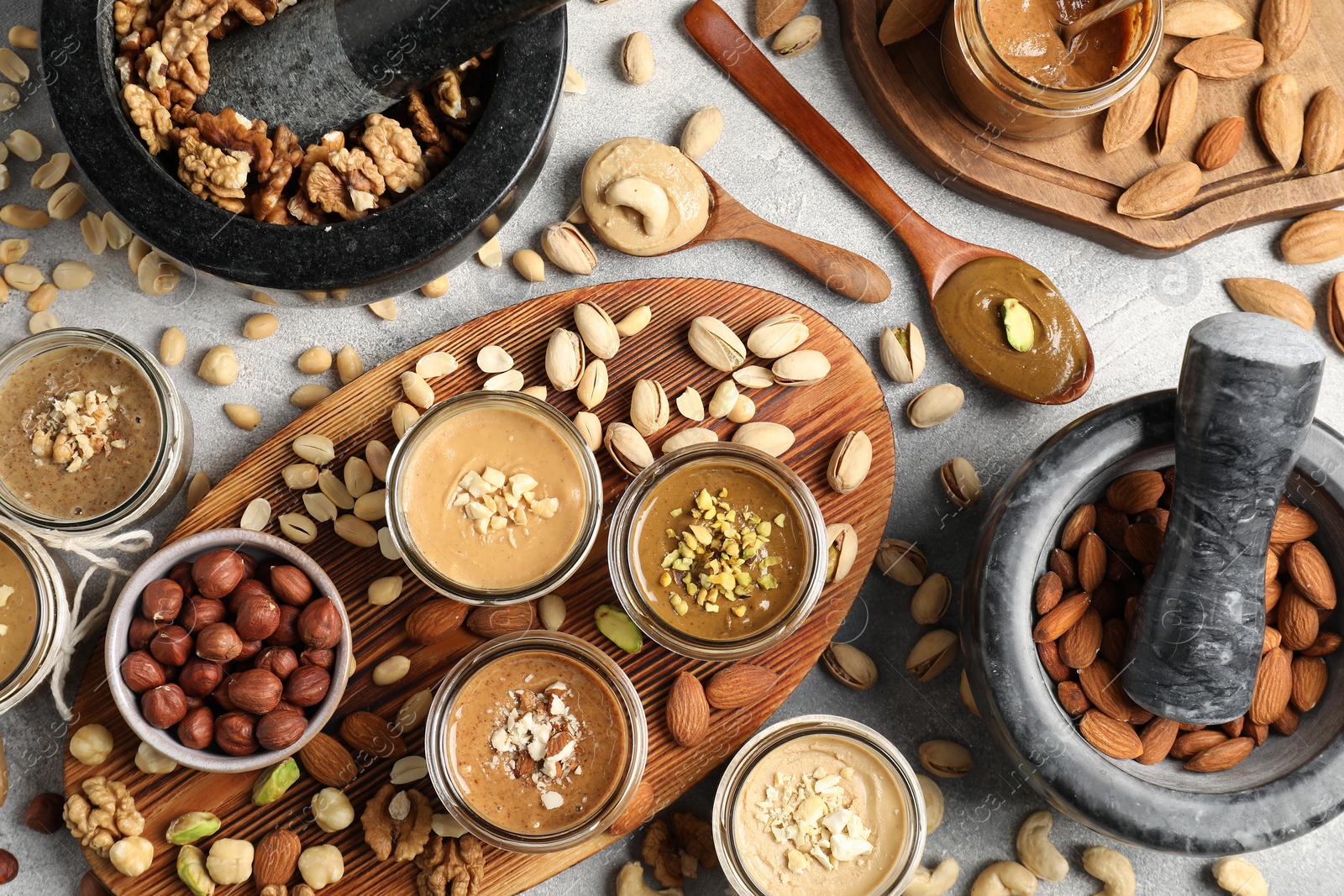 Photo of Making nut butters from different nuts. Flat lay composition on light grey table