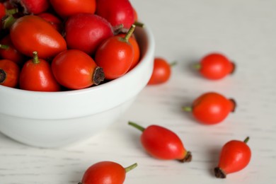 Photo of Ripe rose hip berries with bowl on white wooden table, closeup. Space for text