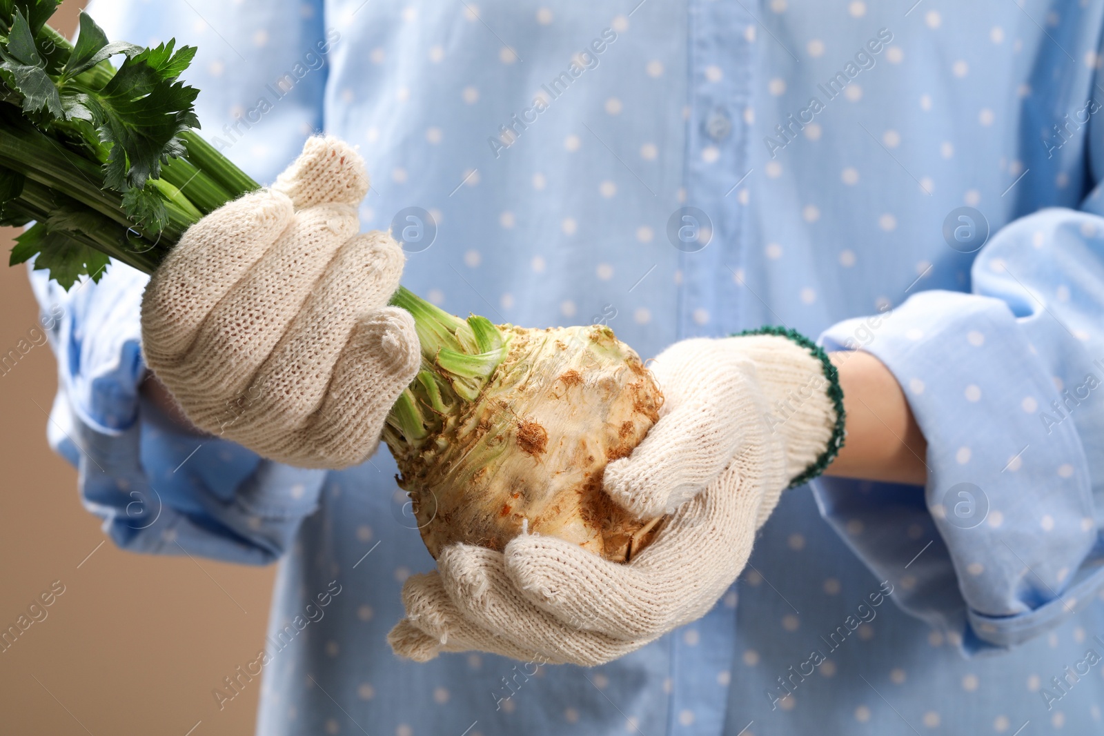 Photo of Woman holding raw celery root on beige background, closeup