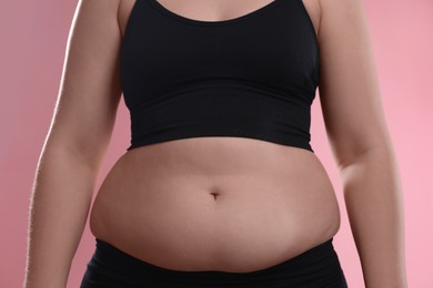 Woman with excessive belly fat on pink background, closeup. Overweight problem