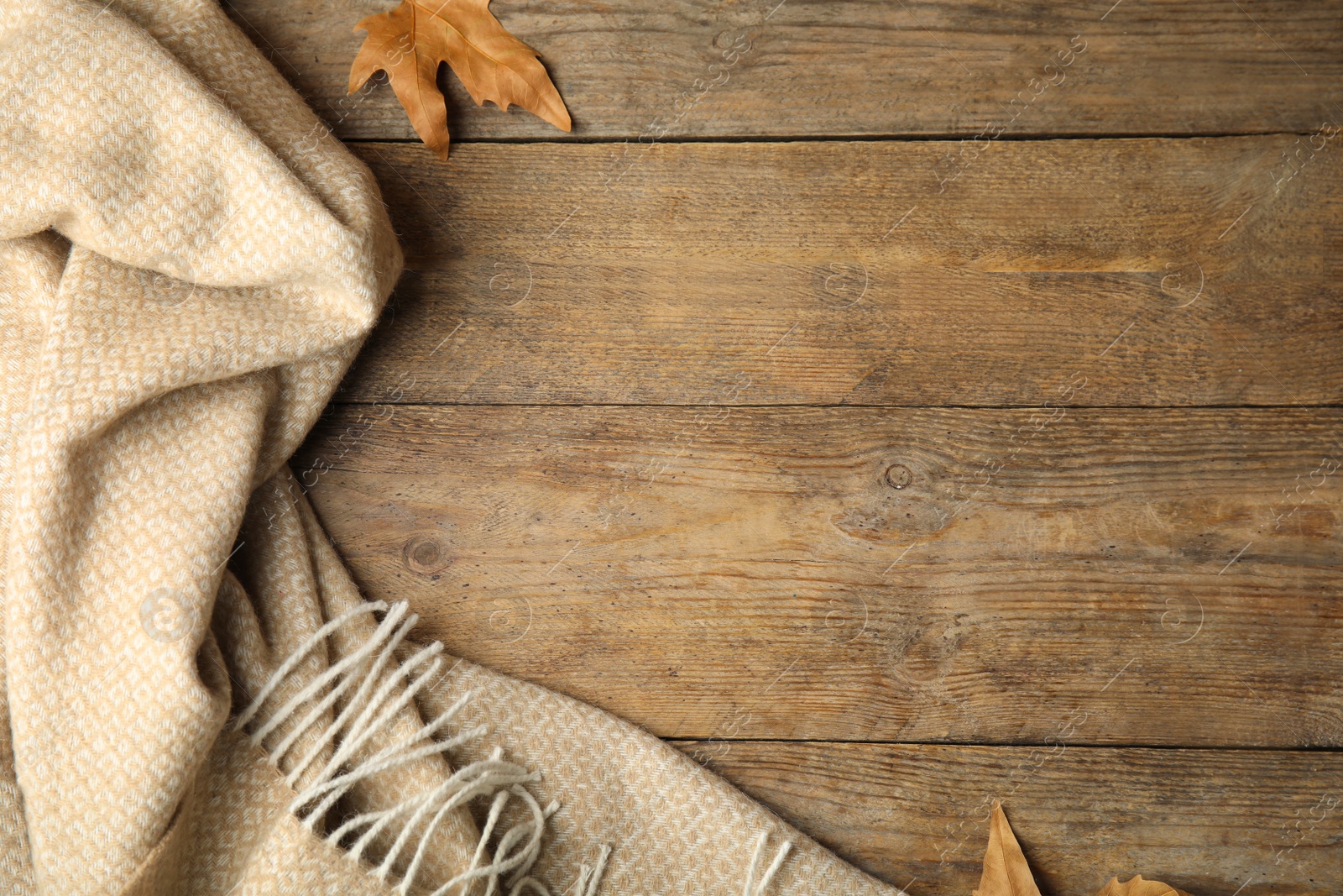 Photo of Beige plaid and dry leaves on wooden table, flat lay. Space for text