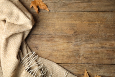 Photo of Beige plaid and dry leaves on wooden table, flat lay. Space for text