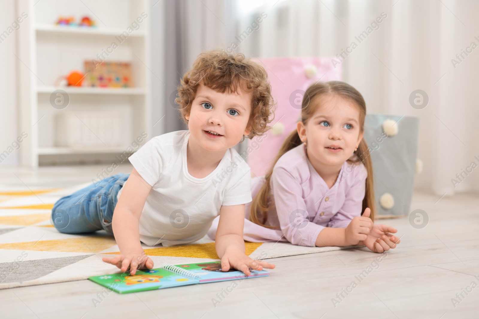 Photo of Cute little children reading book on floor in kindergarten