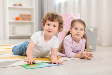 Cute little children reading book on floor in kindergarten